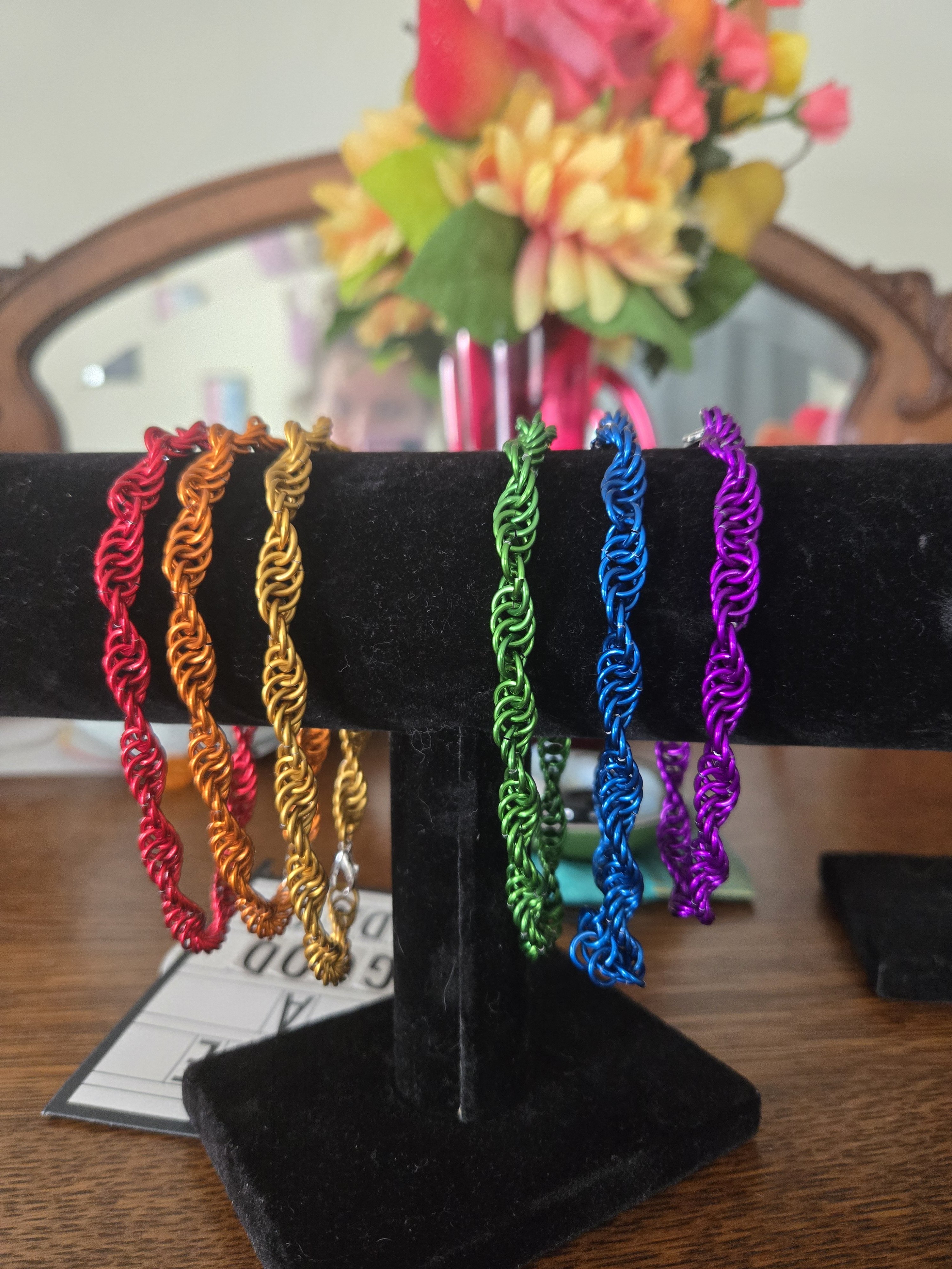 Six spiral bracelets on a black display stand. The bracelets are made of shiny colored metal in a helix pattern. The bracelets are each a different color of the rainbow.