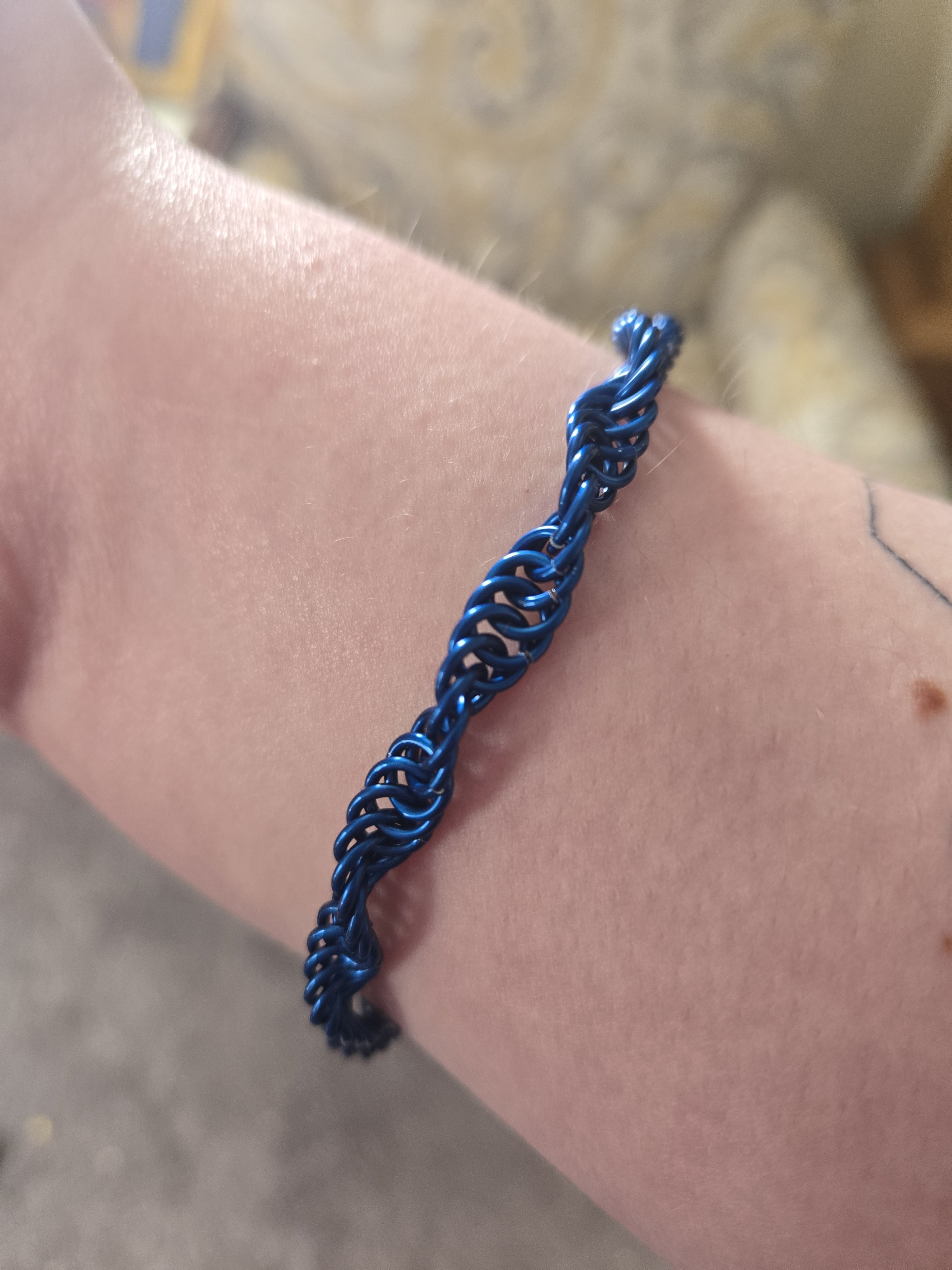 A blue bracelet on a wrist. The bracelet is made up of shiny blue metal rings in a helix pattern.