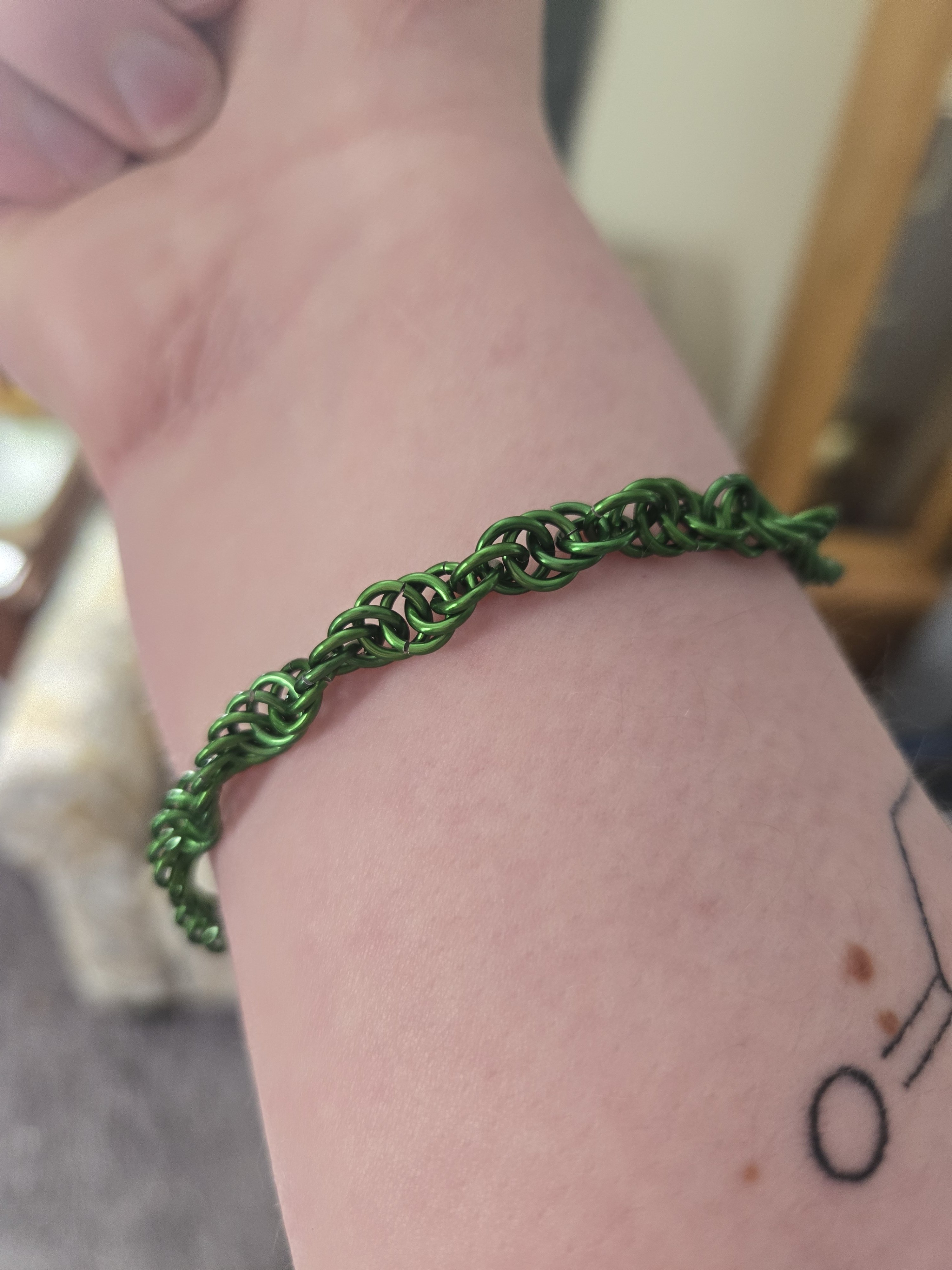 A green bracelet on a wrist. The bracelet is made up of shiny green metal rings in a helix pattern.