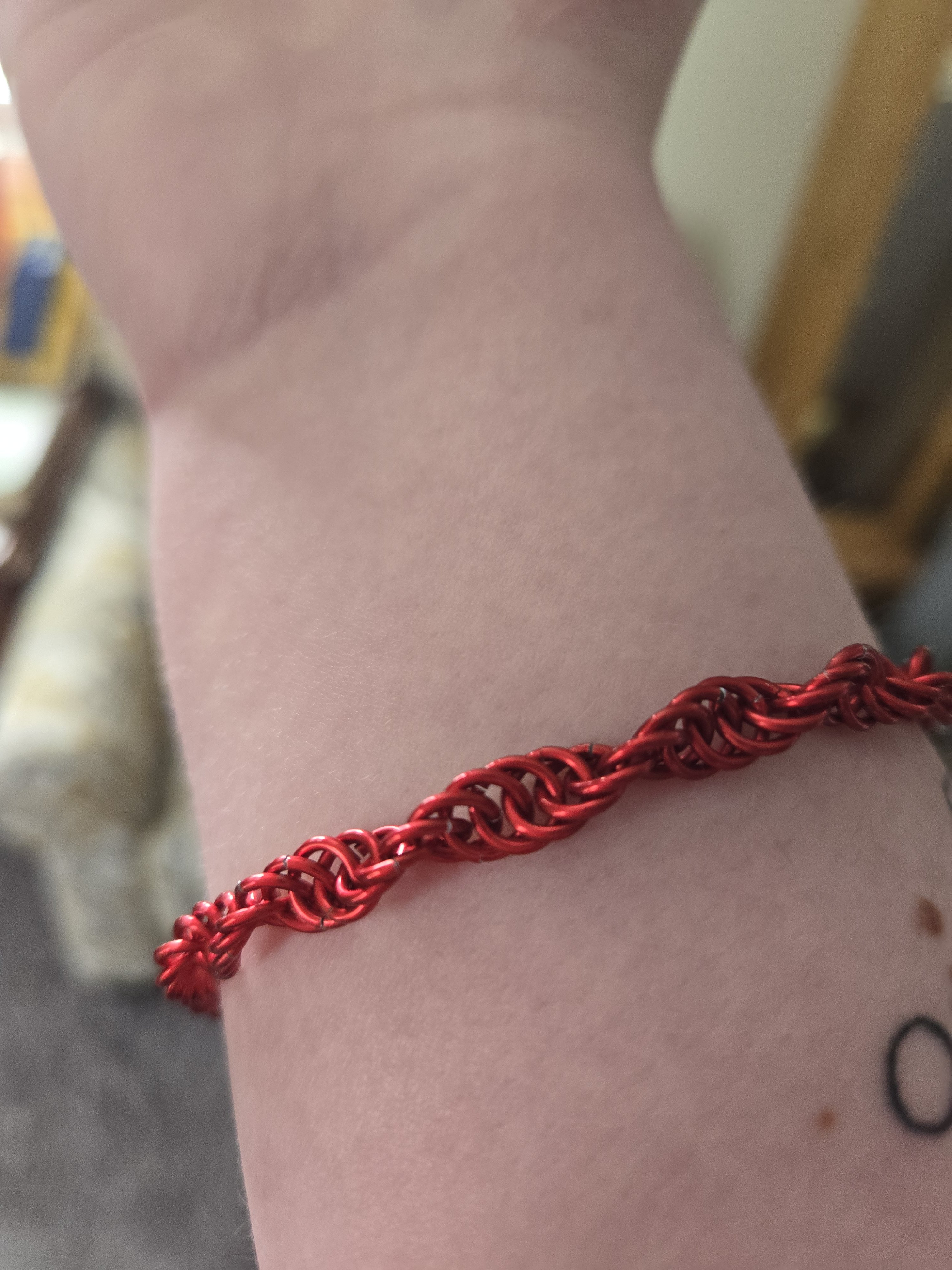 A red bracelet on a wrist. The bracelet is made up of shiny red metal rings in a helix pattern.