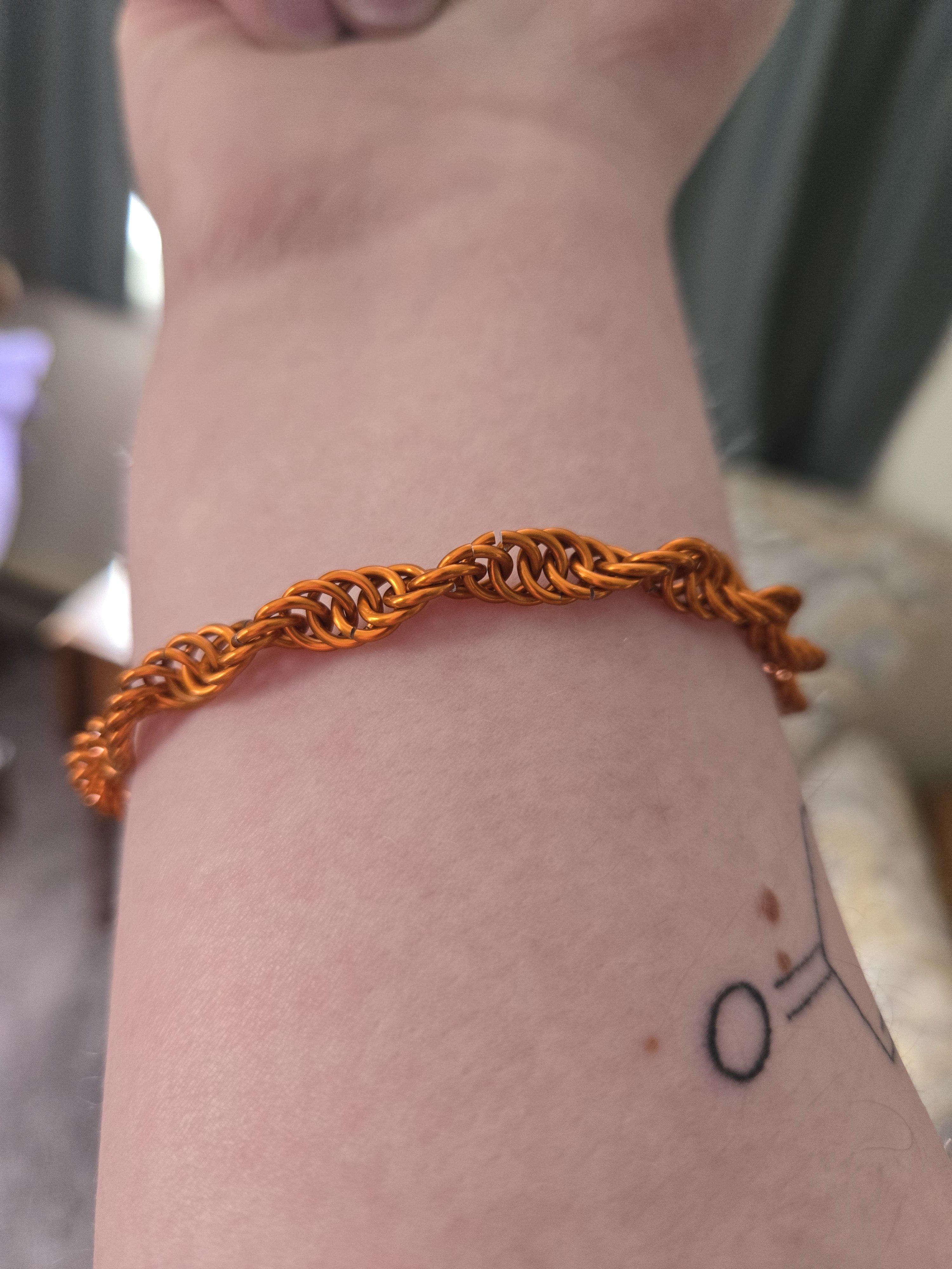 A orange bracelet on a wrist. The bracelet is made up of shiny orange metal rings in a helix pattern.